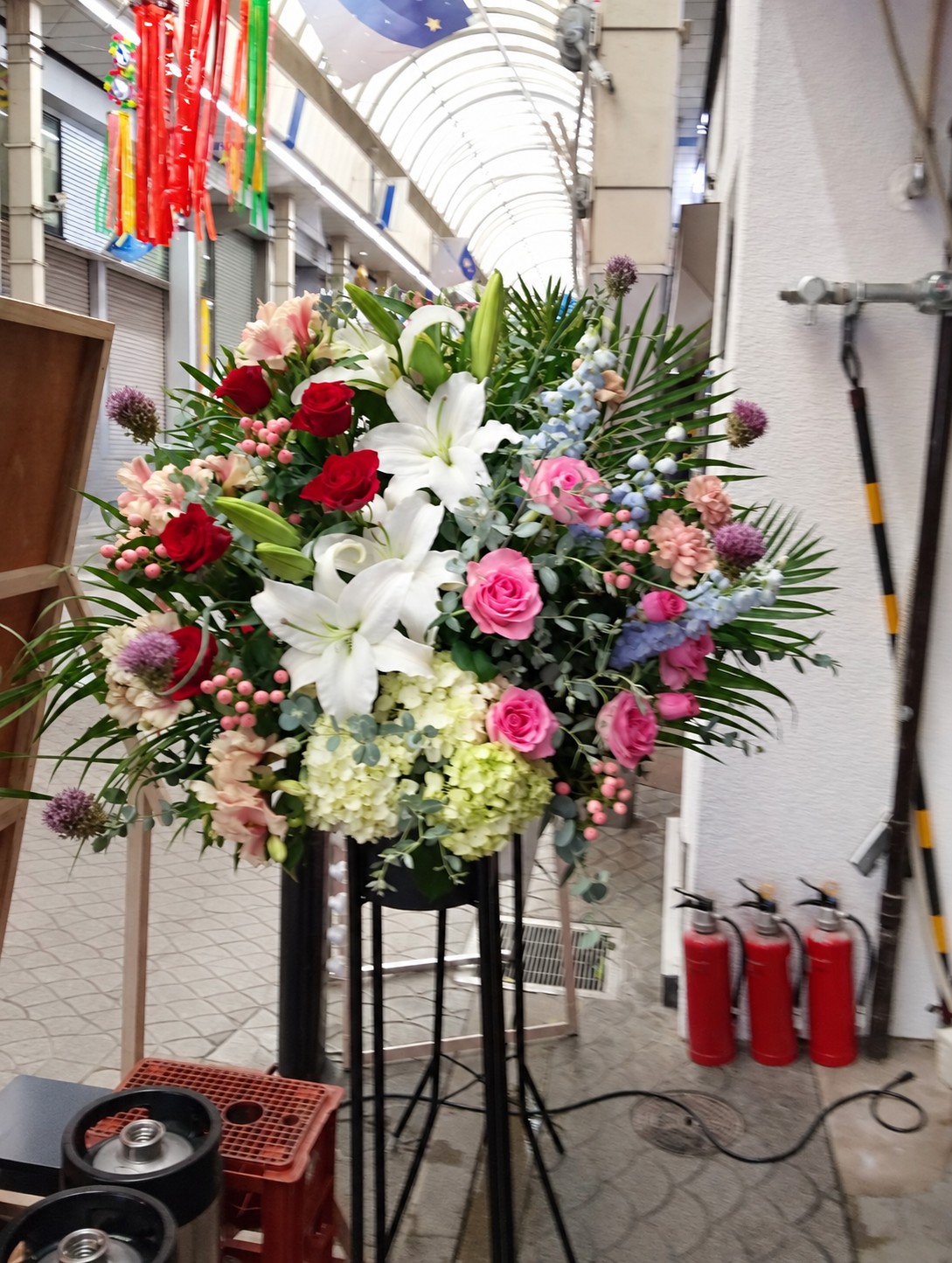赤とピンクのバラ、白いユリ、淡いグリーンのお花のスタンド花