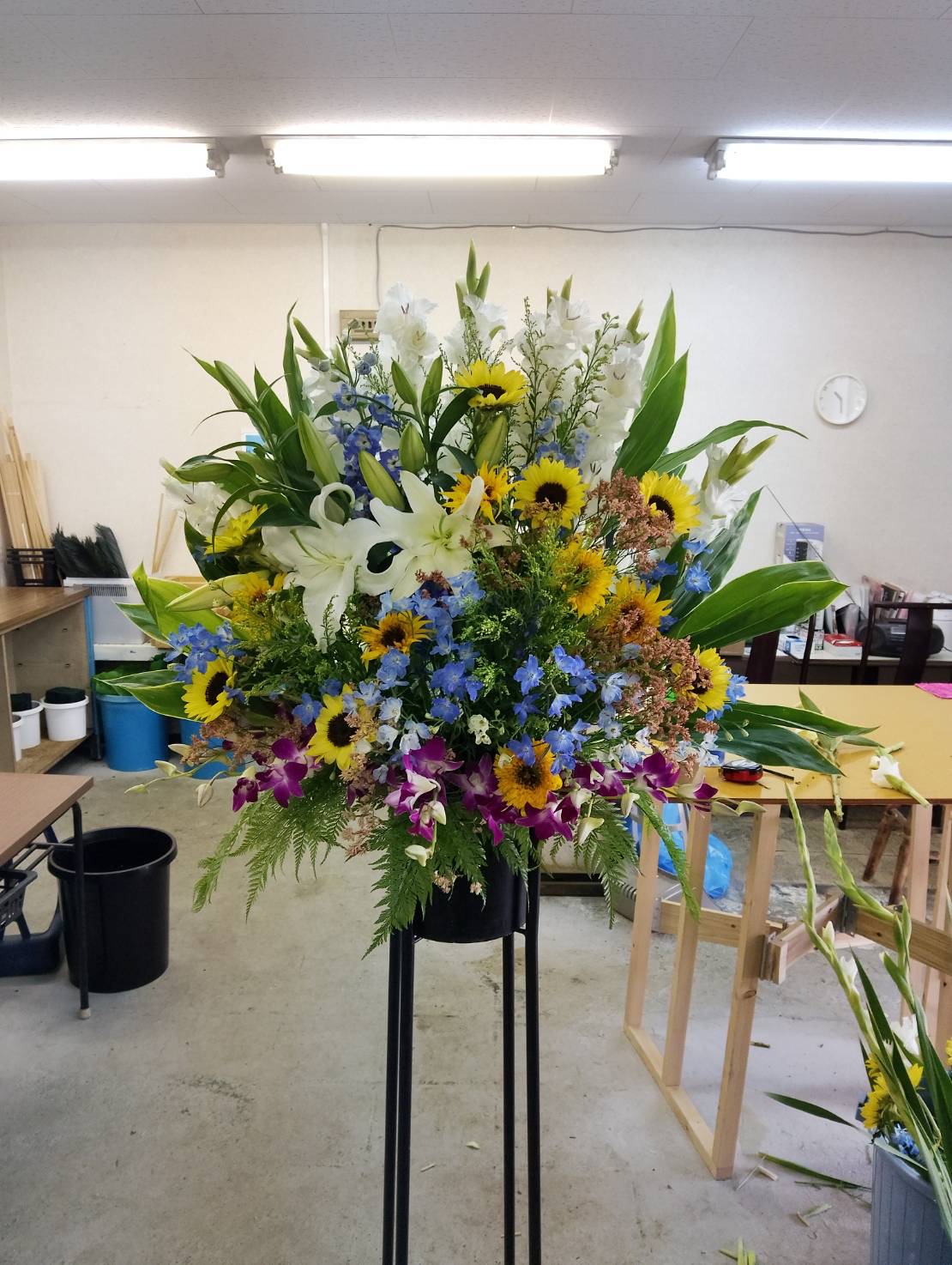 ひまわりと白いユリ、青いお花を合わせたスタンド花