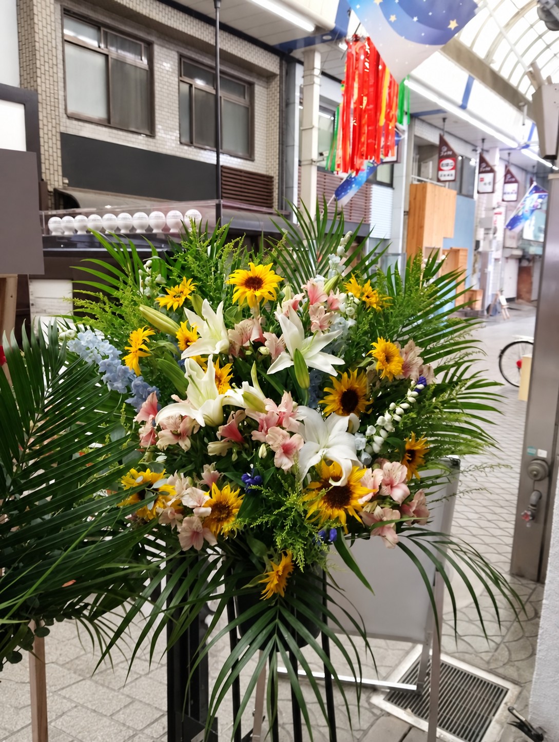 ひまわりと白いユリ、淡いピンクのお花を合わせた開店祝いのスタンド花